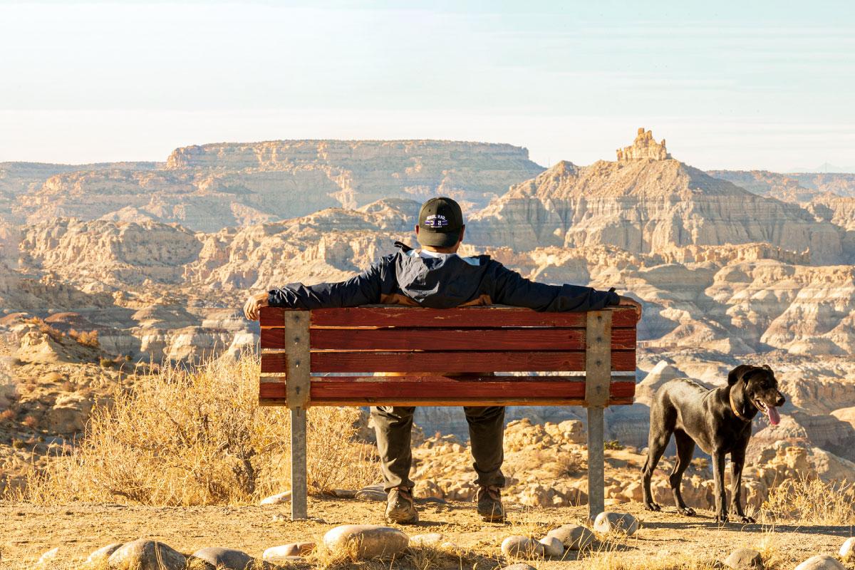 Black dog and person sitting on bench looking at Angel Peak
