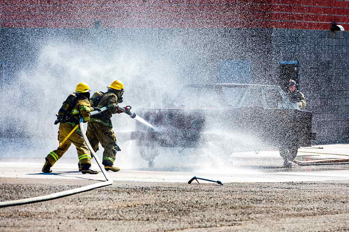 Two firemen practices putting out a vehicle fire at the fire science practice tower.