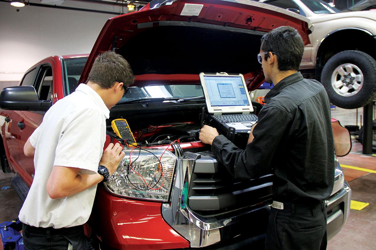 Two students looking under the hood of a pickup.