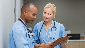 Two people wearing scrubs, looking over a medical chart.